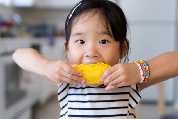 Happy cute little Asian girl eating mango with funny face